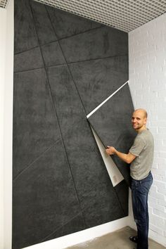 a man standing in front of a black and white wall holding a piece of paper