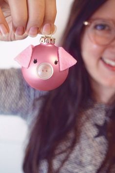 a woman holding a pink pig ornament in her right hand and smiling at the camera