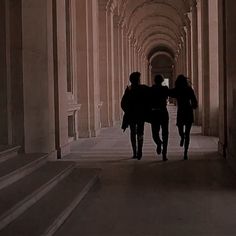 three people walking down a long hallway between two sets of stone pillars with columns on either side