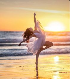 a woman is dancing on the beach at sunset