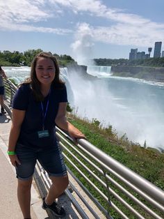 a woman standing on the side of a bridge next to a river with a waterfall in the background