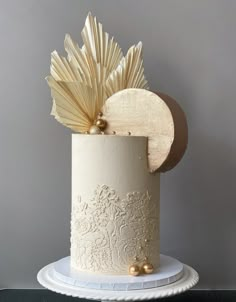 a white wedding cake with gold decorations on the top and sides, sitting on a pedestal