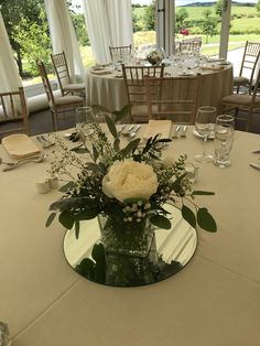 a vase with flowers on a table at a wedding reception in front of a large window