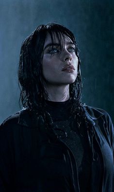 a woman with wet hair standing in front of a dark background and looking off to the side