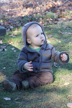 a small child sitting on the grass with a frisbee in his hand and wearing a hoodie