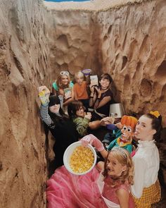 a group of children in costumes are sitting on the ground and eating popcorn from bowls