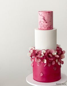 a three tiered pink and white cake with flowers on the top, sitting on a plate