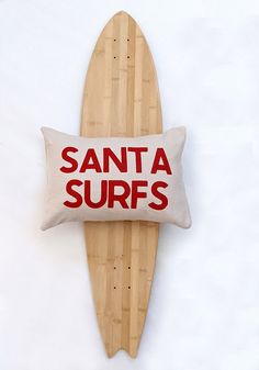 a wooden surfboard with a santa surfing pillow on it's side that says, santa surfs