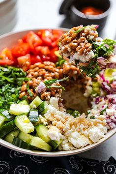 a bowl filled with different types of salads and dressing on top of a table