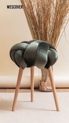 a green chair sitting on top of a white carpet next to a vase with dry grass