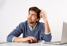 a man sitting at a desk with a laptop and cell phone in front of him