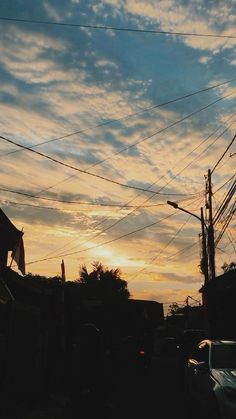 the sun is setting behind power lines and telephone poles in an urban area with cars parked on the street