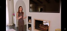 a woman standing in front of a fireplace with her hands out to the side and looking at the camera