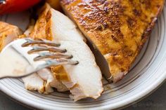 a white plate topped with sliced up chicken next to a fork and pepper on top of it