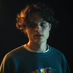 a young man with curly hair standing in the dark