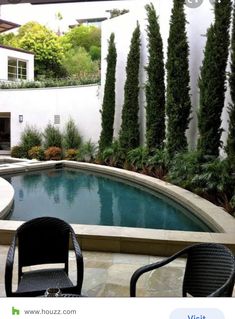 two chairs sitting in front of a pool surrounded by greenery and trees on the side of a house