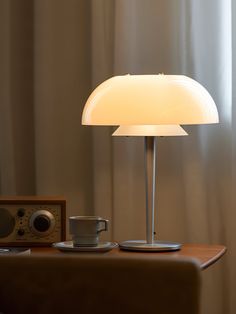 a table lamp sitting on top of a wooden table next to a cup and radio