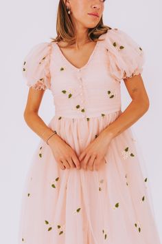 Fall in love with our EXCLUSIVE - Our Love Story Dress! This light blush dress is adorned with white flowers and features a v-neckline, puff sleeves, and decorative buttons on the front bodice. The invisible back zipper and midi length add the perfect touches. Perfect for a romantic date or a playful picnic! Details Light blush dress decorated with white flowers decorative buttons down front of bodice Invisible zipper in back Puff sleeves with elastic on ends Midi length V-neckline Comes in size Cute Puff Sleeve Wedding Dresses, Blush Dress For Spring Garden Party, Spring Bridesmaid Dresses With Puff Sleeves, Cute V-neck Dress For Garden Party, Cute Fitted Peach Dress, Peach Puff Sleeve Fitted Dress, Cute V-neck Garden Party Dresses, Blush Short Sleeve Spring Dress, Blush Short Sleeve Dress For Spring