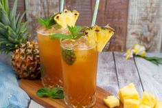 two glasses filled with pineapple juice and garnished with mint on a cutting board