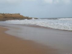 people are walking on the beach near the water and sand cliffs, with waves crashing in to shore