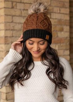 a woman wearing a brown and black hat with two pom poms on it