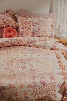 a bed with pink and orange floral comforter set on it's headboard