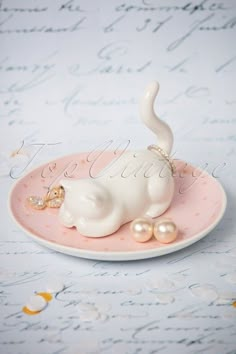 a white cat figurine sitting on top of a pink plate with pearls around it