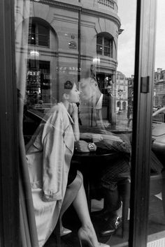 a man and woman sitting at a table in front of a store window, kissing