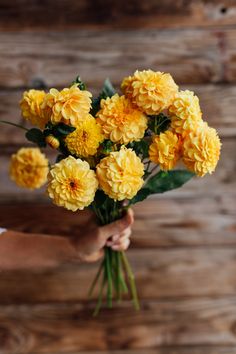 a person holding a bunch of yellow flowers in their hands on a wooden wall background