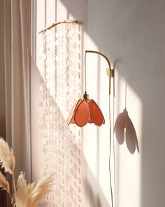 two lamps on the wall next to a window with white curtains and a plant in front