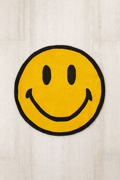 a yellow smiley face rug on a white wall with black trim around the eyes and nose