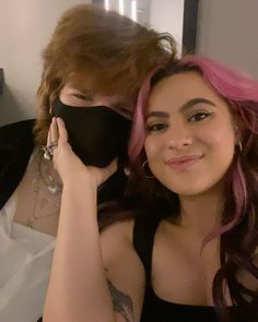 two women with pink hair and black masks on their faces, one is holding a cell phone to her ear