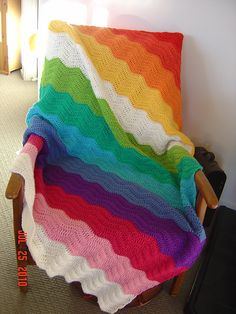 a rainbow blanket sitting on top of a wooden chair next to a wall in a room