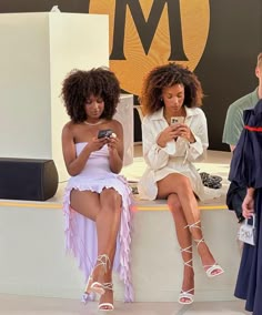 three women sitting on a bench looking at their cell phones in front of the m logo