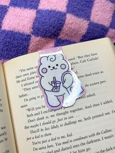 an open book with a bear sticker on the pages and a purple checkered blanket behind it