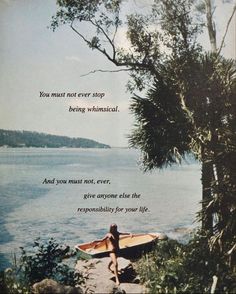 a woman sitting on a rock next to a body of water with a surfboard