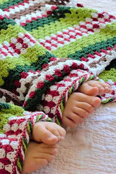 a baby laying on top of a bed covered in a crocheted blanket with feet sticking out