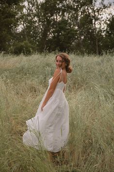 a woman in a white dress walking through tall grass