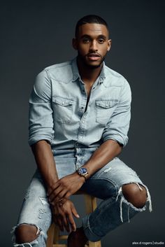 a man sitting on top of a wooden stool wearing ripped jeans and a denim shirt