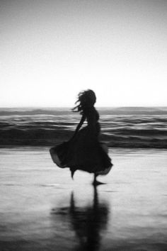 a woman in a long dress is walking on the beach with her hair blowing in the wind