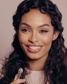 a woman with long curly hair holding a brush in her right hand and smiling at the camera