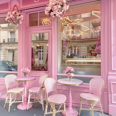 a pink cafe with chairs and tables in front of the storefront, filled with flowers