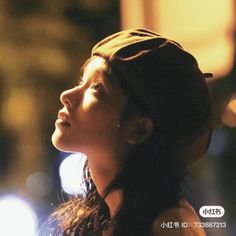 a woman with long hair wearing a beanie looking up at something in the distance