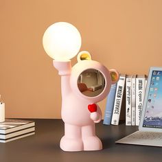 a pink lamp with a bear holding a light bulb on it's head next to a laptop