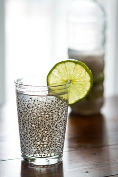 a glass filled with water next to a lime slice on top of a wooden table