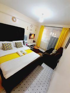 a bed with yellow and white pillows in a bedroom next to a window, chair