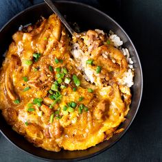 a black bowl filled with rice and chicken covered in gravy next to a spoon