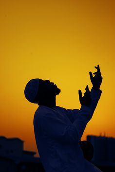 the silhouette of a man with his hands in the air, against an orange and yellow sky