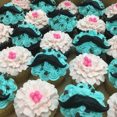 cupcakes with blue frosting and pink flowers in the shape of mustaches