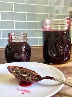 a spoon full of jam sitting on top of a white plate next to a jar